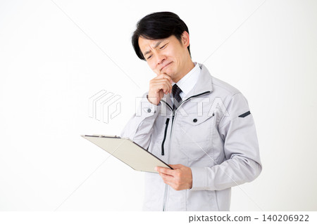 一位身穿灰色工作服的中年商人,在白色背景下,正看著一疊文件,思考著他的工作。 一位身穿灰色工作服的中年商人,在白色背景下,正看著一疊文件,思考著他的工作。 140206922