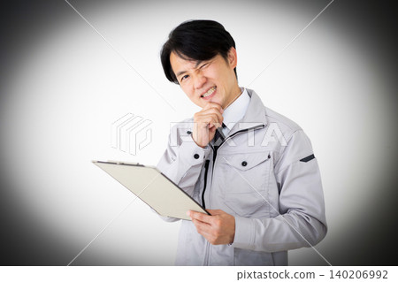 一位身穿灰色工作服的中年商人,在白色背景下,正看著一疊文件,思考著他的工作。 一位身穿灰色工作服的中年商人,在白色背景下,正看著一疊文件,思考著他的工作。 140206992