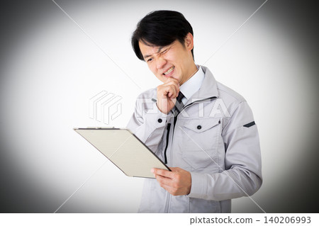 A middle-aged businessman in gray work clothes is looking at a binder of documents, with a white background. A middle-aged businessman in gray work clothes is looking at a binder of documents, with a white background. 140206993
