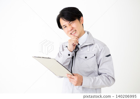 A middle-aged businessman in gray work clothes is looking at a binder of documents, with a white background. A middle-aged businessman in gray work clothes is looking at a binder of documents, with a white background. 140206995