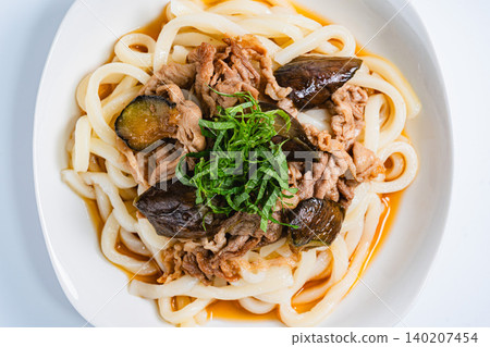 A photo of a chilled udon noodle dish with eggplant and pork, topped with shiso leaves, perfect for summer. A photo of a chilled udon noodle dish with eggplant and pork, topped with shiso leaves, perfect for summer. 140207454