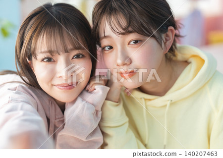 Two young women smiling with their faces close together. 140207463