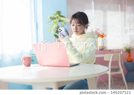 一位年輕女子一邊使用筆記型電腦，一邊操作智慧型手機。 140207523