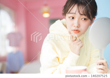 A young woman seriously checks the condition of her skin in the mirror. A young woman seriously checks the condition of her skin in the mirror. 140207525