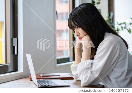 一位日本女性在辦公室裡看著筆記型電腦,陷入沉思。 一位日本女性在辦公室裡看著筆記型電腦,陷入沉思。 140207572