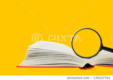A magnifying glass rests on a book, bright yellow backdrop A magnifying glass rests on a book, bright yellow backdrop 140207762