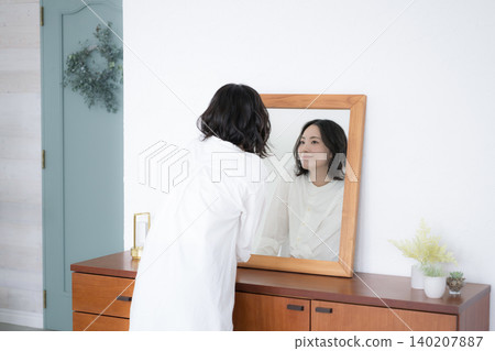 女性的生活方式:在鏡子前整理儀容-上半身,背部視角。 女性的生活方式:在鏡子前整理儀容-上半身,背部視角。 140207887