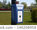 Emergency call box with camera and flashing light mounted on a pole beside a grassy park and campus building. A blue alarm station provides safety and emergency communication 140208958