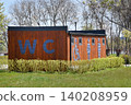 Accessible public restroom with wheelchair symbol along a park pathway. Park-side WC with accessible facilities beside flowering trees for visitors. 140208959