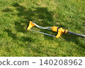 A yellow lawn sprinkler waters grass in a backyard. The sprinkler irrigates the green lawn, capturing spring garden care. 140208962