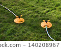 Two yellow oscillating sprinklers water a lush green lawn in a backyard garden. Backyard garden sprinklers irrigate grass on a bright summer day, evoking spring and summer holidays. 140208967