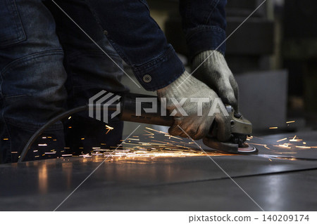 The hand where sparks fly as a metal plate is ground with a disc grinder. The hand where sparks fly as a metal plate is ground with a disc grinder. 140209174