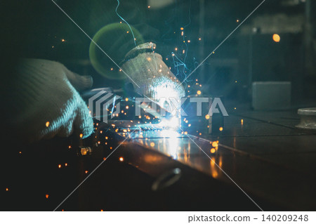 In a dimly lit workshop, the hands performing semi-automatic welding, the pale blue arc and sparks... In a dimly lit workshop, the hands performing semi-automatic welding, the pale blue arc and sparks... 140209248
