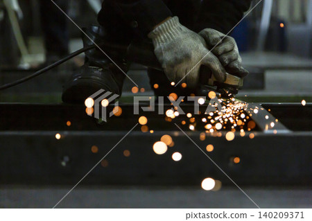 The process of grinding metal with a disc grinder, causing orange sparks to fly. The process of grinding metal with a disc grinder, causing orange sparks to fly. 140209371