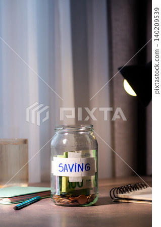 Close up of coins being added to transparent money jar. Represents traditional saving methods and conscious money management for future security Close up of coins being added to transparent money jar. Represents traditional saving methods and conscious money management for future security 140209539