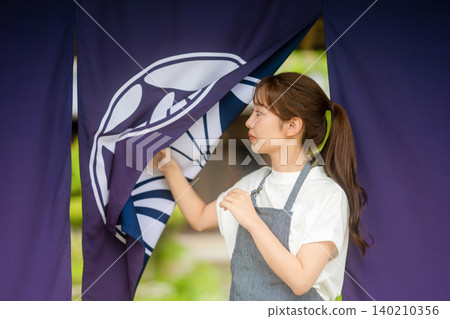 A woman who handles the noren (curtain) for a traditional Japanese house cafe. A woman who handles the noren (curtain) for a traditional Japanese house cafe. 140210356