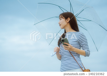 A woman holding an umbrella and a smartphone 140210362