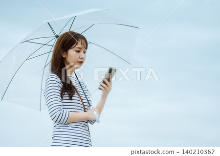 一位撐著傘的女子正在操作智慧型手機 一位撐著傘的女子正在操作智慧型手機 140210367