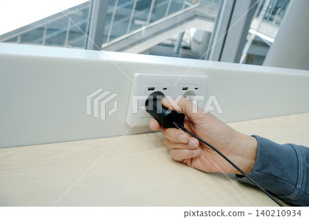 a man plugs a charger into a wall outlet a man plugs a charger into a wall outlet 140210934
