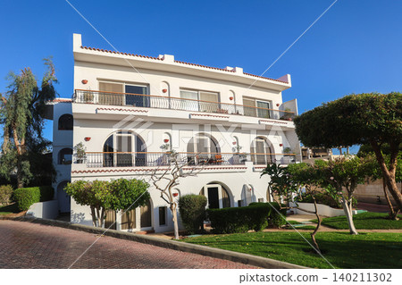Modern residential apartment building surrounded by palm trees in an Arab country under clear blue sky 140211302