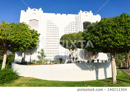 Modern residential apartment building surrounded by palm trees in an Arab country under clear blue sky 140211304