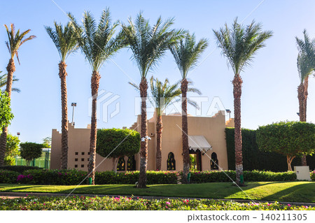 Modern residential apartment building surrounded by palm trees in an Arab country under clear blue sky 140211305