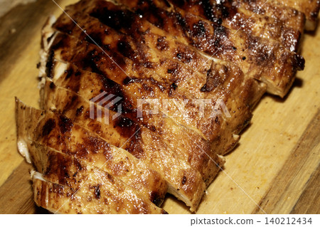 Close up of sliced roasted and glazed chicken breast on a wooden chopping board 140212434