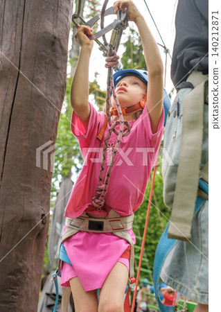 A girl in close-up moves a carabiner along a rope while passing a suspended rope track in an outdoor amusement park A girl in close-up moves a carabiner along a rope while passing a suspended rope track in an outdoor amusement park 140212871