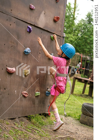 A child in a safety helmet with a safety rope climbs the wall of a climbing wall in an outdoor recreation park. Healthy lifestyle A child in a safety helmet with a safety rope climbs the wall of a climbing wall in an outdoor recreation park. Healthy lifestyle 140212951