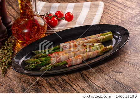 Grilled bacon wrapped asparagus appetizer on black plate with flavored oil and cherry tomatoes Grilled bacon wrapped asparagus appetizer on black plate with flavored oil and cherry tomatoes 140213199