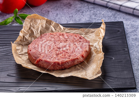 Raw hamburger patty on parchment paper ready for cooking with fresh basil and tomatoes Raw hamburger patty on parchment paper ready for cooking with fresh basil and tomatoes 140213309