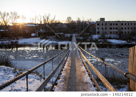 A suspension bridge over the Msta River in winter, on a sunny day. Borovichi, Novgorod Oblast, Russia. A suspension bridge over the Msta River in winter, on a sunny day. Borovichi, Novgorod Oblast, Russia. 140214812
