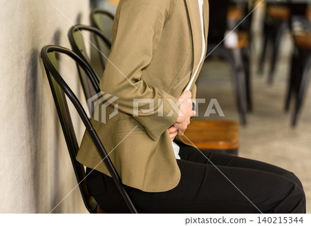 A woman is sitting in a chair and holding her stomach. A woman is sitting in a chair and holding her stomach. 140215344