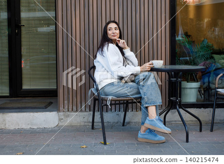 Smiling woman drinking coffee in city street cafe outdoors Smiling woman drinking coffee in city street cafe outdoors 140215474