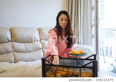 Portrait of woman with tangerines in a fruit box at home. Organic harvest and fruit storage Portrait of woman with tangerines in a fruit box at home. Organic harvest and fruit storage 140215475