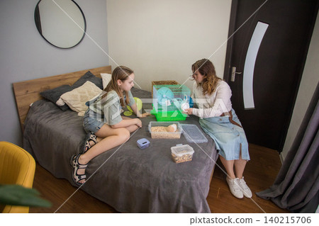 young girl and an adult are in a bedroom preparing a hamster cage. They are talking young girl and an adult are in a bedroom preparing a hamster cage. They are talking 140215706