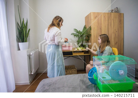 Two people are cleaning a hamster cage. One person is sitting on a bed while the other is a table. Two people are cleaning a hamster cage. One person is sitting on a bed while the other is a table. 140215711