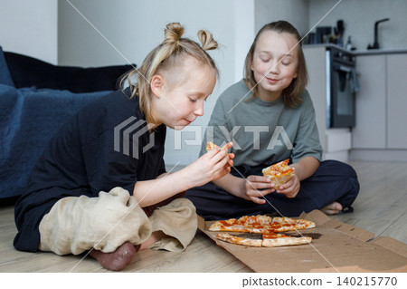 Joyful young children sitting on floor in living room and eating pizza at home 140215770