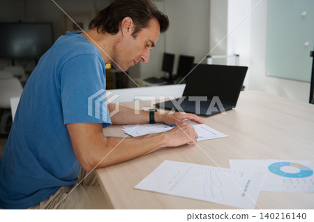 Man focused on work, analyzing charts while working on laptop in co-working office Man focused on work, analyzing charts while working on laptop in co-working office 140216140