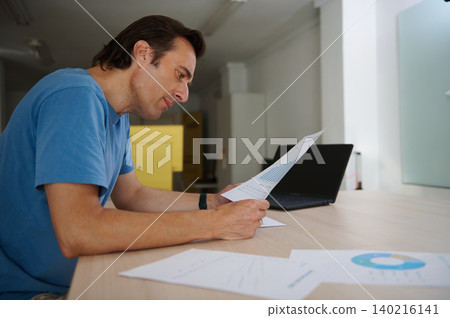 Man focused on work, analyzing charts while working on laptop in co-working office Man focused on work, analyzing charts while working on laptop in co-working office 140216141