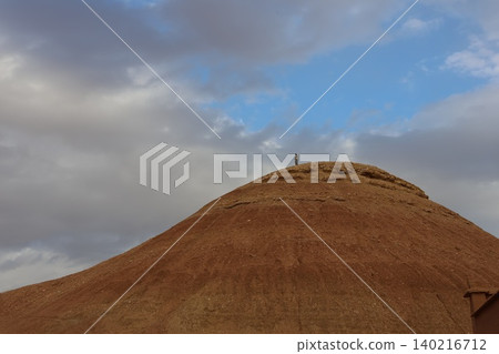 Single person stands atop large earthen mound under cloudy sky Single person stands atop large earthen mound under cloudy sky 140216712