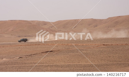 A rugged off-road vehicle drives across a vast desert landscape, leaving a long trail of dust behind it. A rugged off-road vehicle drives across a vast desert landscape, leaving a long trail of dust behind it. 140216717