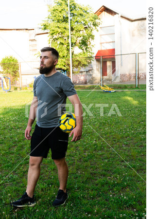 Man with beard holding soccer ball outdoors, near a building. Man with beard holding soccer ball outdoors, near a building. 140216820