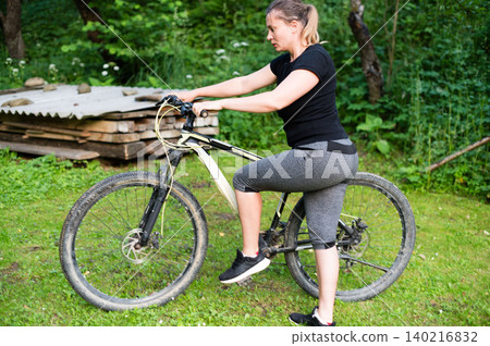 Woman preparing to ride her mountain bike outdoors on a grassy area. 140216832