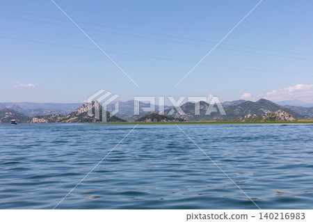 Wide view of Lake Skadar shoreline and mountains under clear blue sky Wide view of Lake Skadar shoreline and mountains under clear blue sky 140216983