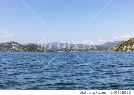 Scenic view across Skadar Lake with mountains and blue sky, Virpazar area Scenic view across Skadar Lake with mountains and blue sky, Virpazar area 140216988
