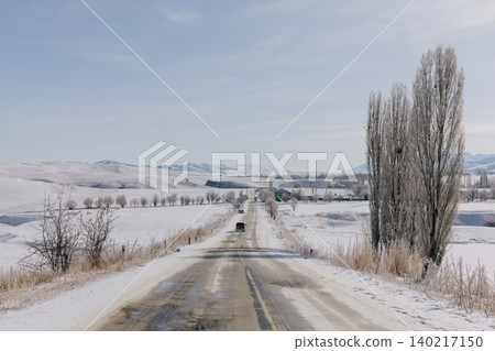 Winter road through snowy countryside landscape in Kyrgyzstan with bare trees Winter road through snowy countryside landscape in Kyrgyzstan with bare trees 140217150
