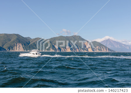 Motor yacht cruising on rough sea near Kamchatka coastline with volcano view Motor yacht cruising on rough sea near Kamchatka coastline with volcano view 140217423