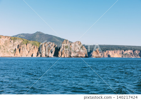 Rocky sea cliffs and coastal mountains on the Kamchatka Peninsula at summer day Rocky sea cliffs and coastal mountains on the Kamchatka Peninsula at summer day 140217424