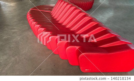 Modern red sculptural bench installed in a minimalist public interior space. Concepts of contemporary design, urban architecture, and creative public furniture. Modern red sculptural bench installed in a minimalist public interior space. Concepts of contemporary design, urban architecture, and creative public furniture. 140218134